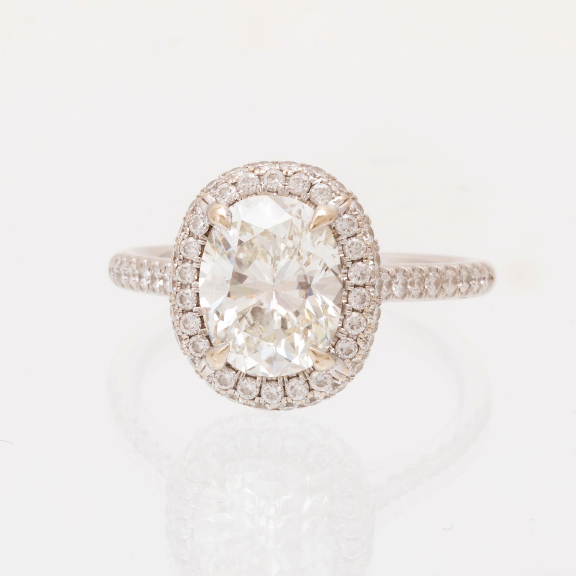 An 18K white gold ring by James Allen, set with an oval brilliant cut diamond in a halo of round brilliant cut diamonds.