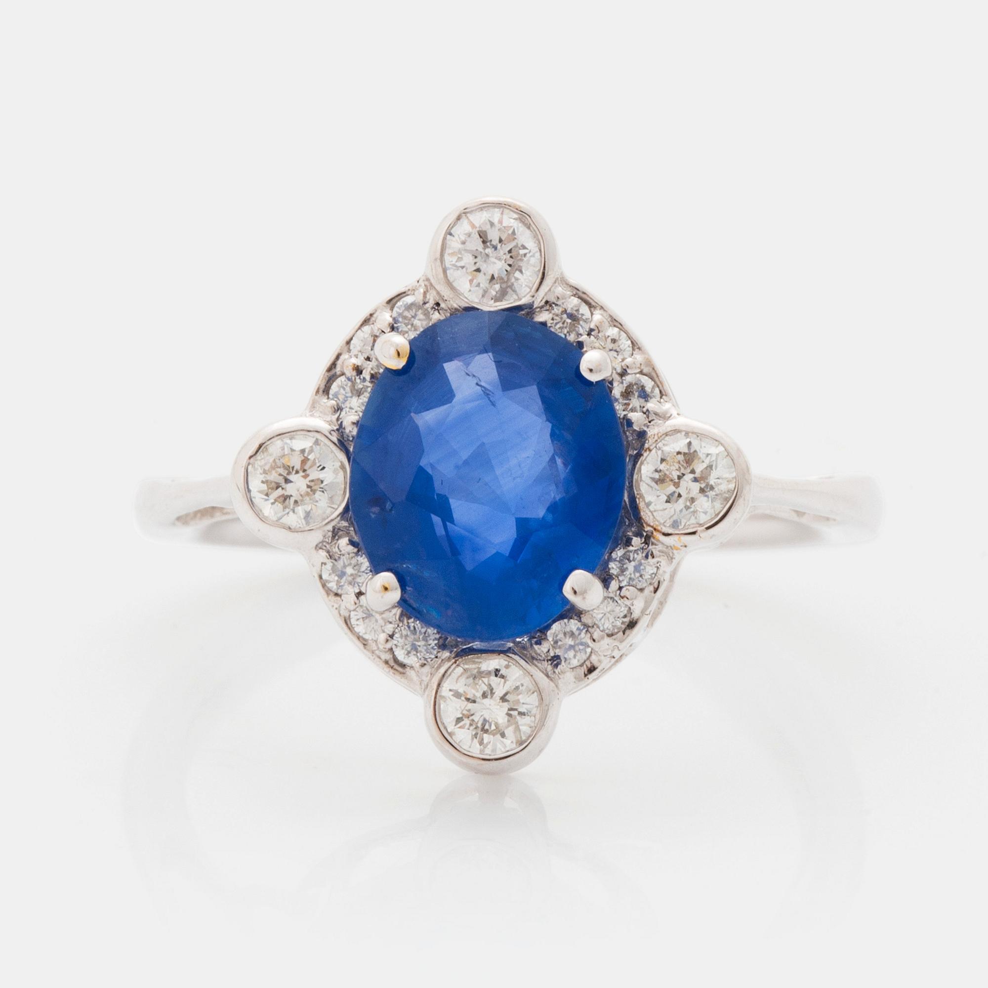 An 18K white gold ring set with a faceted sapphire and round brilliant-cut diamonds.