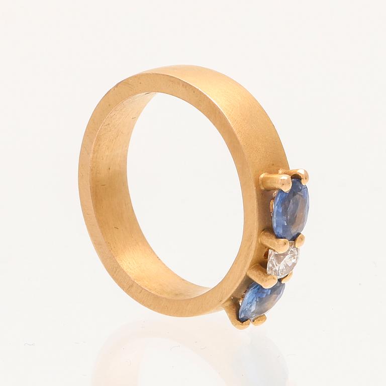 A ring containing at least 21.6K gold, set with a round cut brilliant diamond and oval brilliant cut sapphires.