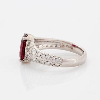 A platinum ring set with a faceted ruby and round brilliant-cut diamonds.