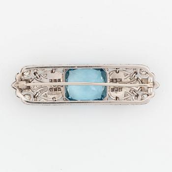 An 18K white gold brooch set with a faceted aquamarine and round brilliant- and rose-cut diamonds.