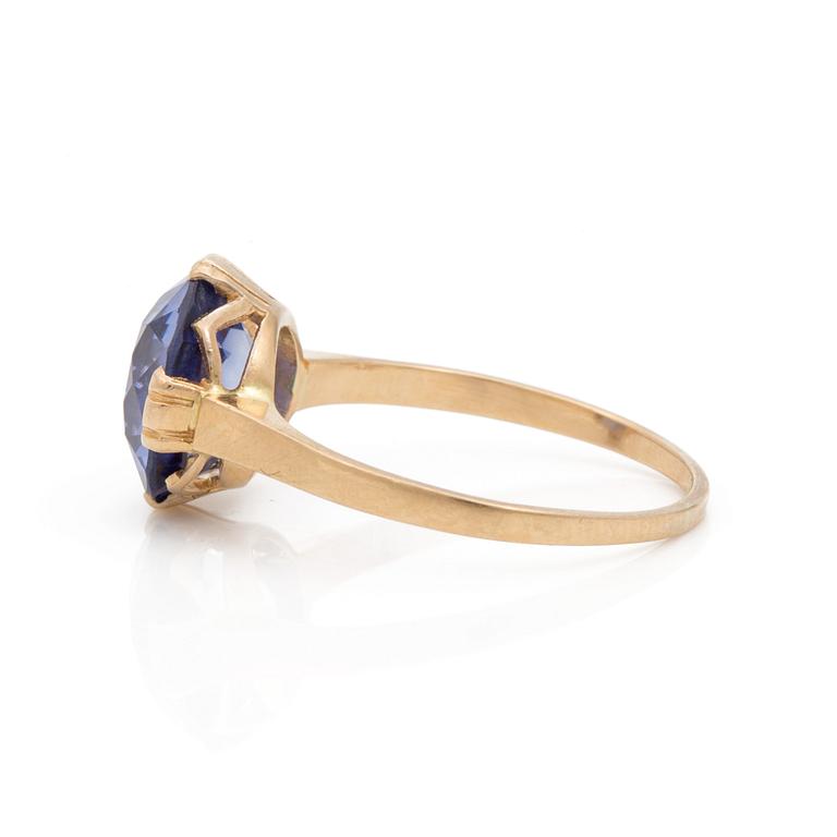 A ring set with a round, mixed-cut, synthetic sapphire.