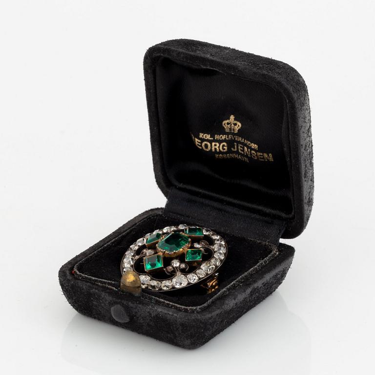 A gold and silver brooch set with faceted emeralds and old- and rose-cut diamonds.