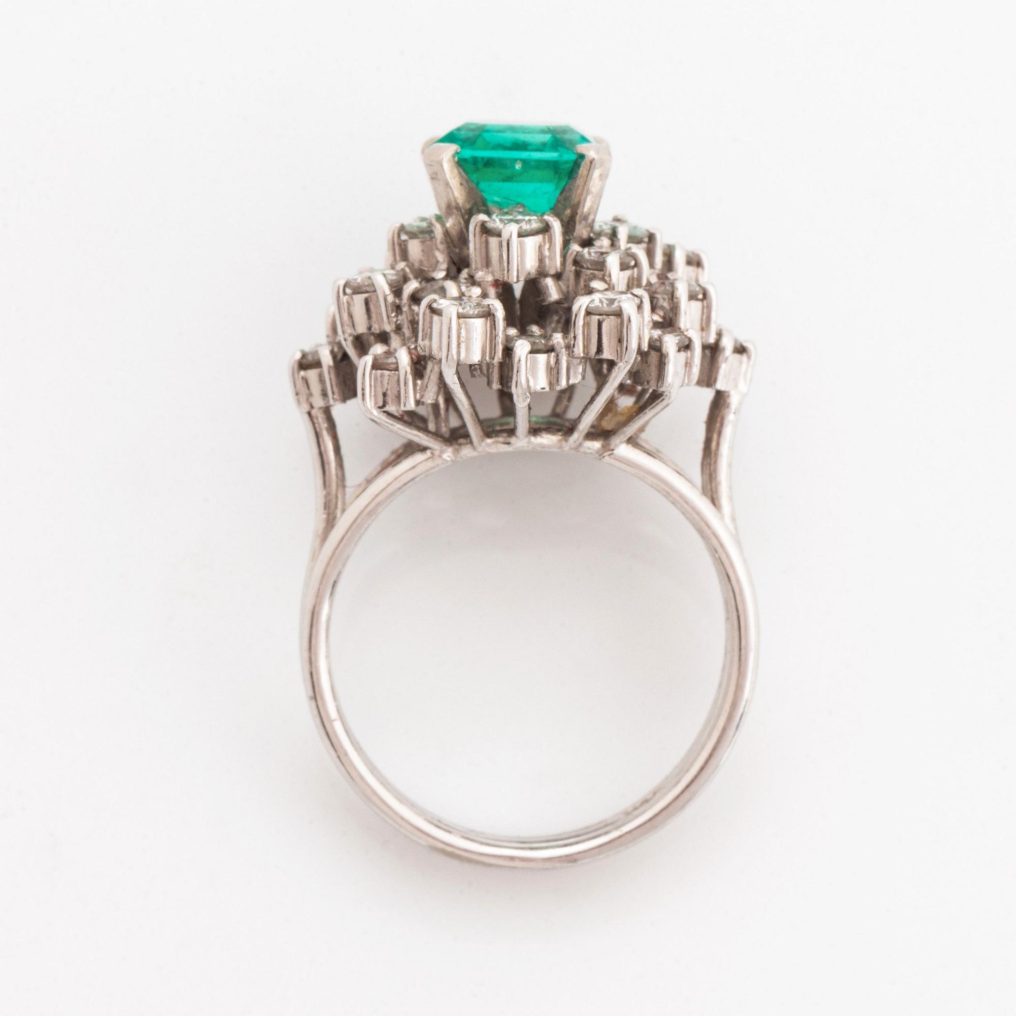 Ring platina med en fasettslipad smaragd och runda briljantslipade diamanter.
