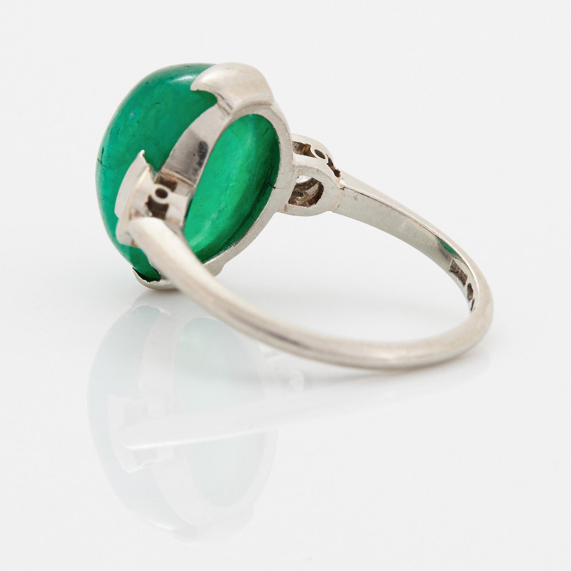 A platinum ring set with a cabochon-cut emerald and round brilliant-cut diamonds.