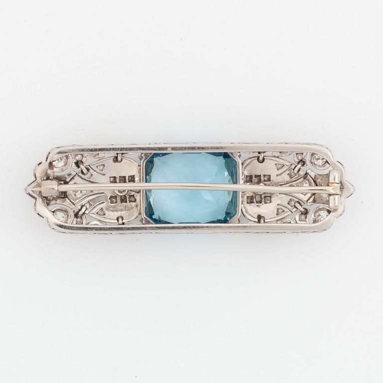 An 18K white gold brooch set with a faceted aquamarine and round brilliant- and rose-cut diamonds.