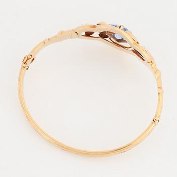 An 18K gold bangle set with a blue synthetic stone.