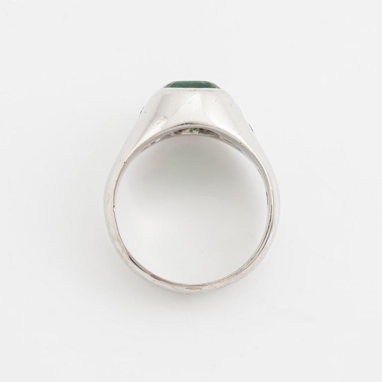 An 18K white old ring set with a faceted emerald and round brilliant-cut diamonds.