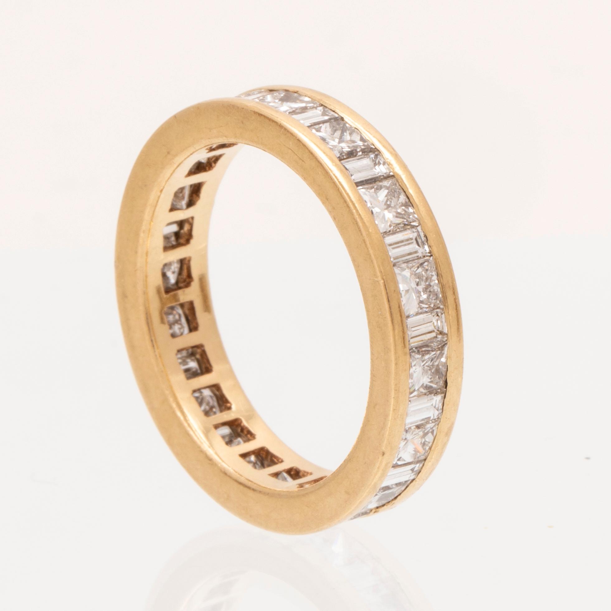 An 18K gold eternity ring set with baguette and princess cut diamonds by Hartmann's Denmark.
