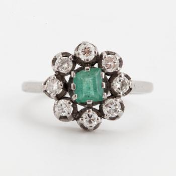 A ring set with a faceted emerald and round brilliant-cut diamonds.