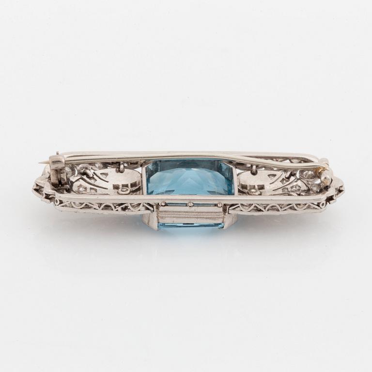 An 18K white gold brooch set with a faceted aquamarine and round brilliant- and rose-cut diamonds.