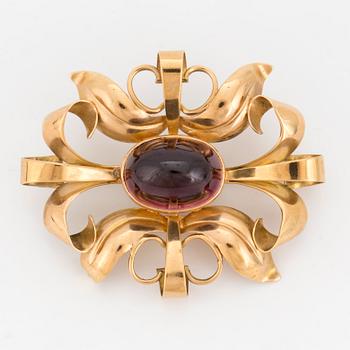 A brooch set with probably a cabochon-cut garnet.