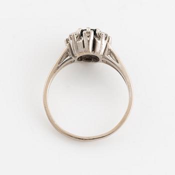 An 18K white gold ring set with a faceted sapphire and round brilliant-cut diamonds.