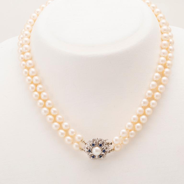 A double-stranded necklace of cultured pearls and an 18K white gold clasp with blue stones.