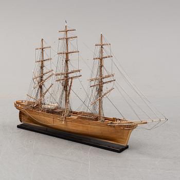 A wooden scale model of Cutty Sark on a painted wooden stand.