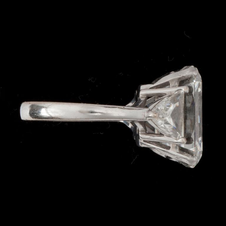A baguette-cut diamond, 9.30 cts, ring. Quality I/VVS2. Flanked by two triangular diamonds approximately 1.00 ct each.