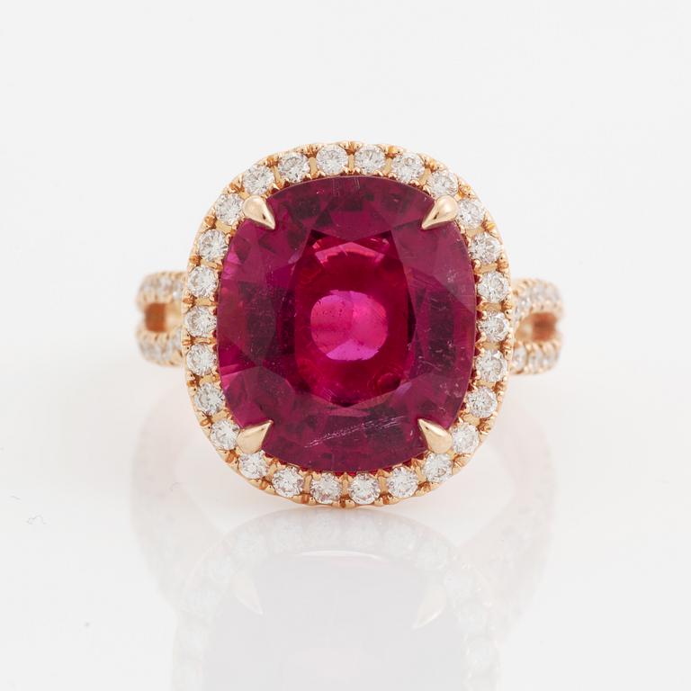 An 18K gold ring set with a faceted pink tourmaline and round brilliant-cut diamonds.