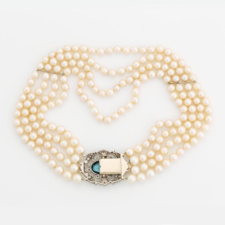 A four strand cultured pearl necklace with a clasp in 14K gold set with a faceted aquamarine.