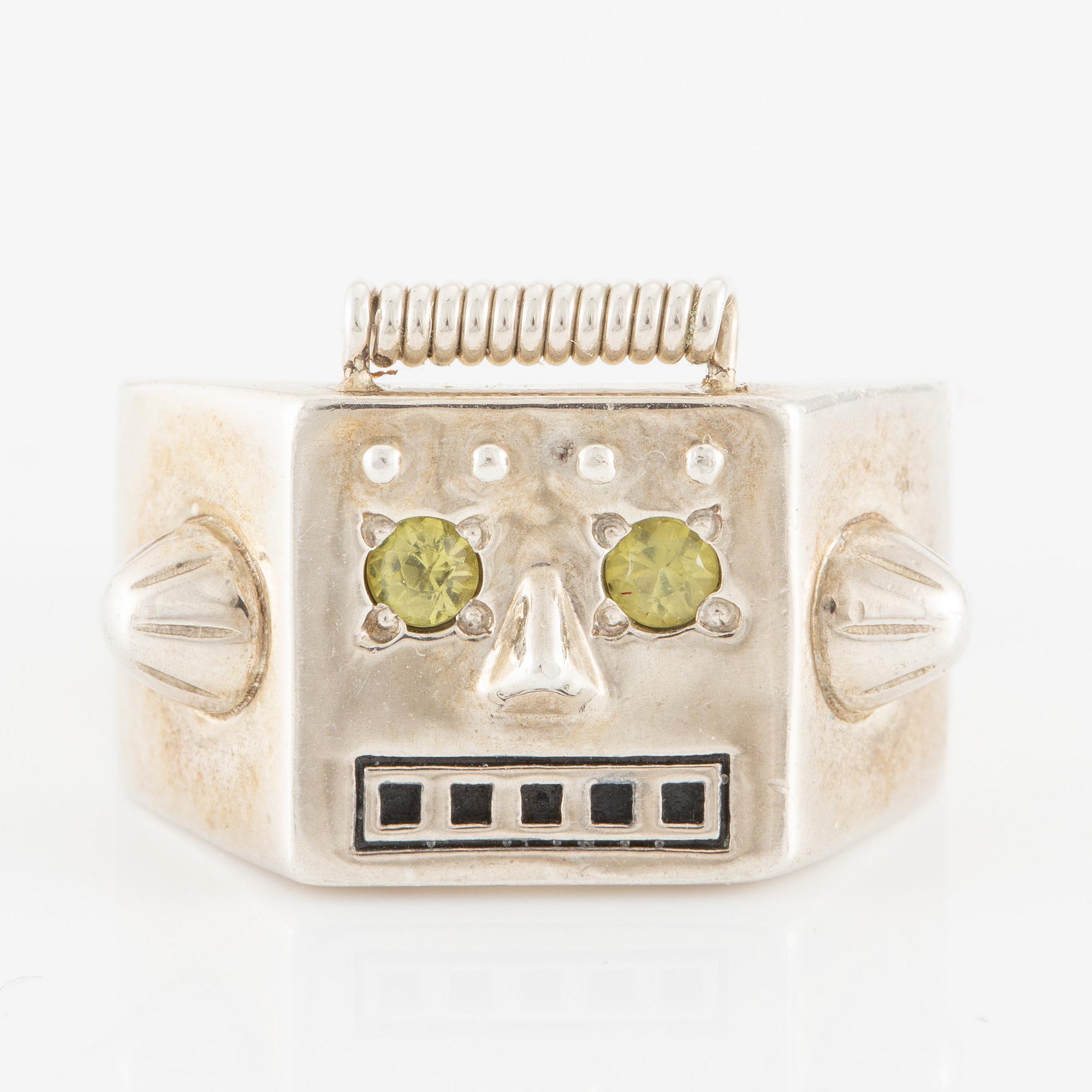 Maria Nilsdotter ring i form av ett robothuvud, sterlingsilver och gröna ögon.