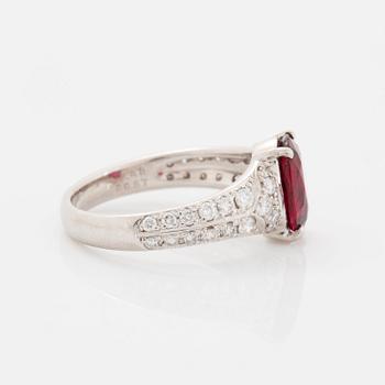 A platinum ring set with a faceted ruby and round brilliant-cut diamonds.