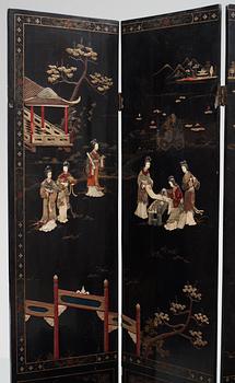 A chinese black lacquer six-panel screen, early 20th Century, with figures in gardens, inlays of carved mother of pearl, coloured bone, tree, and different stones. Back of panels with flowers painted in gold.