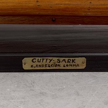 A wooden scale model of Cutty Sark on a painted wooden stand.