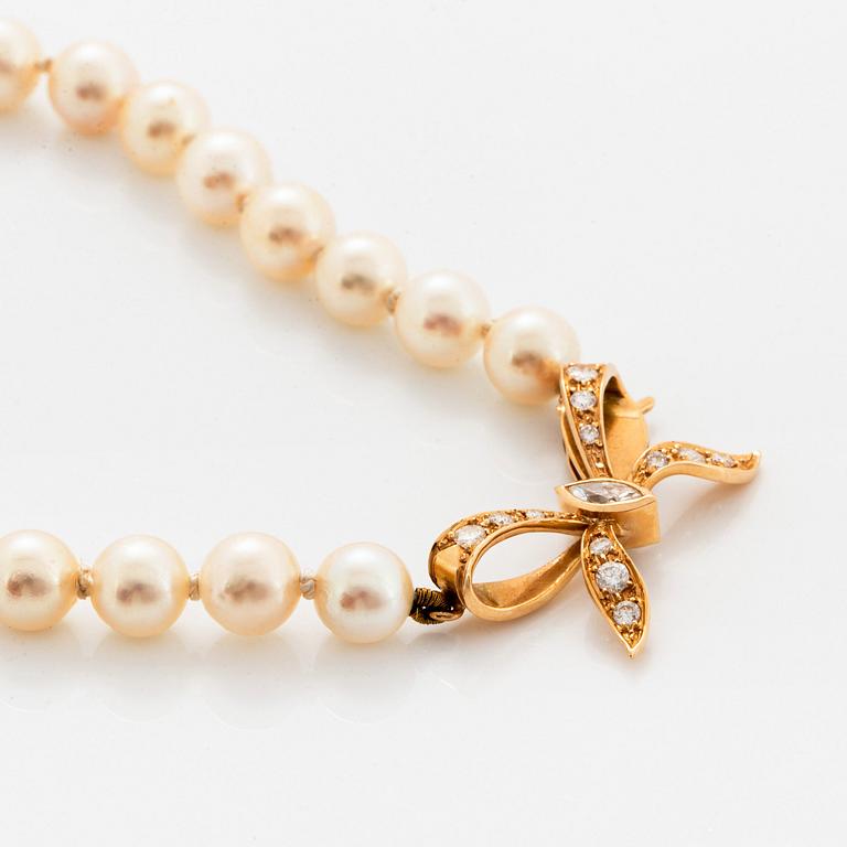 A cultured pearl necklace with a bow clasp in 18K gold set with round brilliant-cut diamonds.