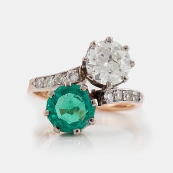 A CROSS-OVER RING set with an old-cut diamond and a round mixed-cut emerald.