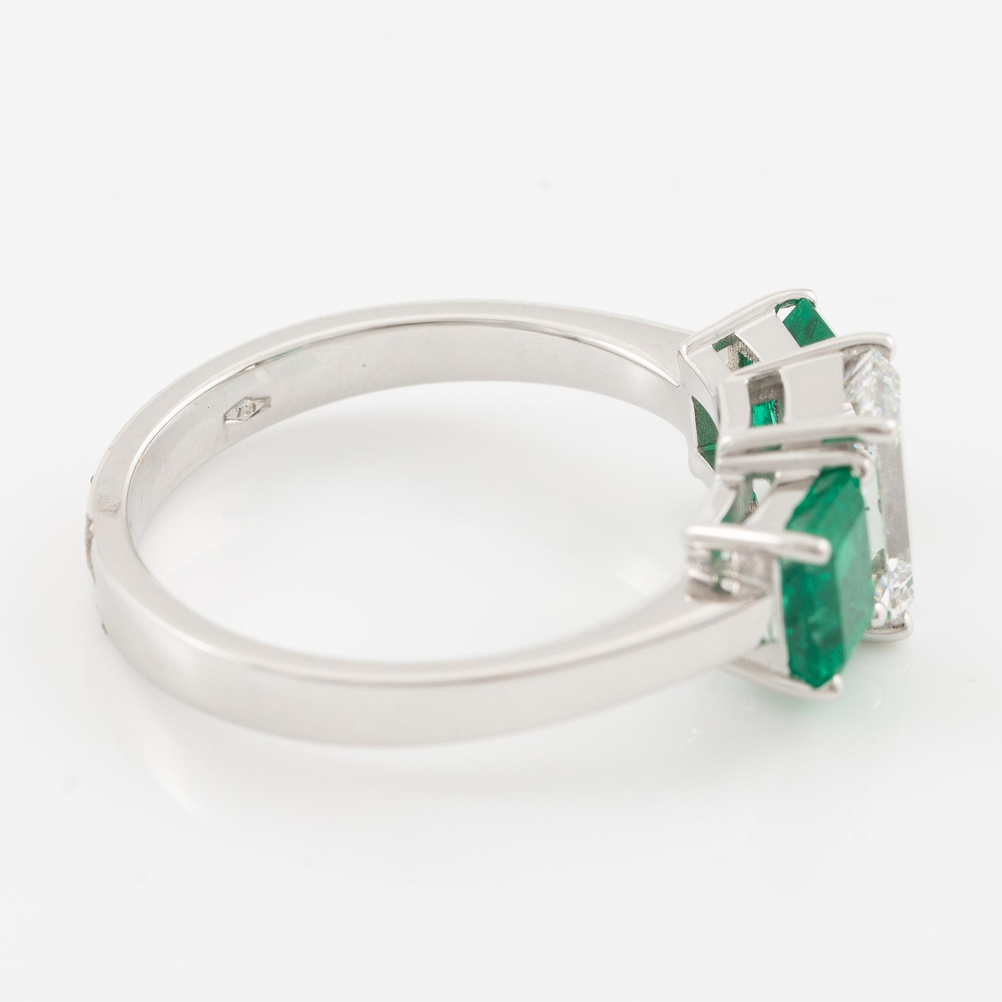An 18K white gold ring set with an emerald-cut diamond and two step-cut emeralds.