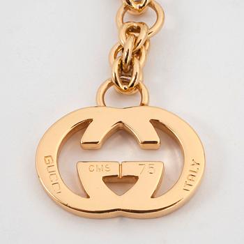 GUCCI, a gold colored mongrammed chain.